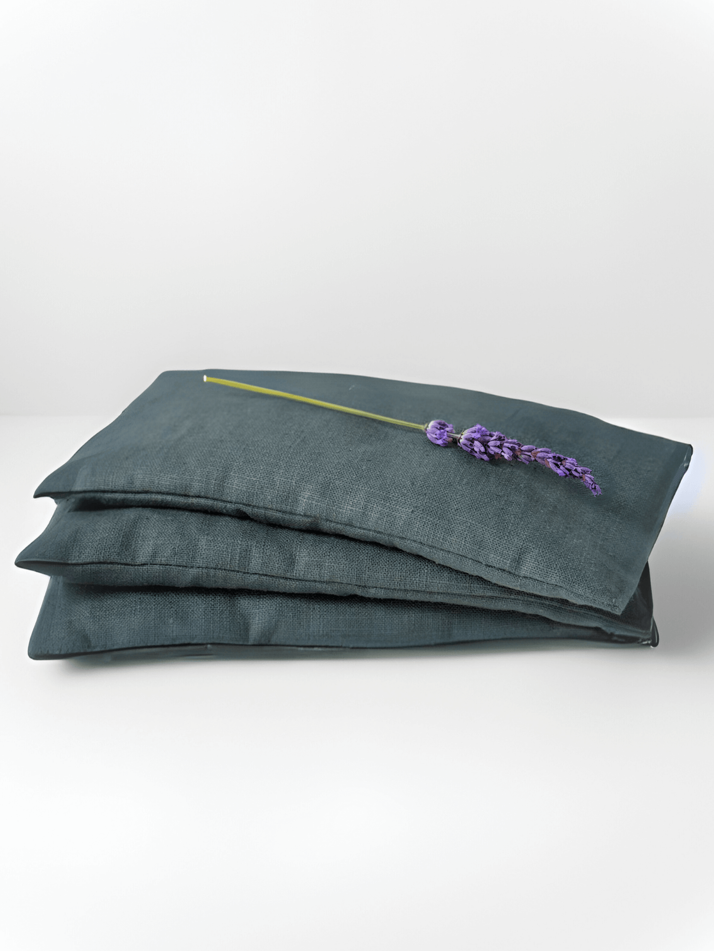 Two grey linen eye pillows stacked on a white background