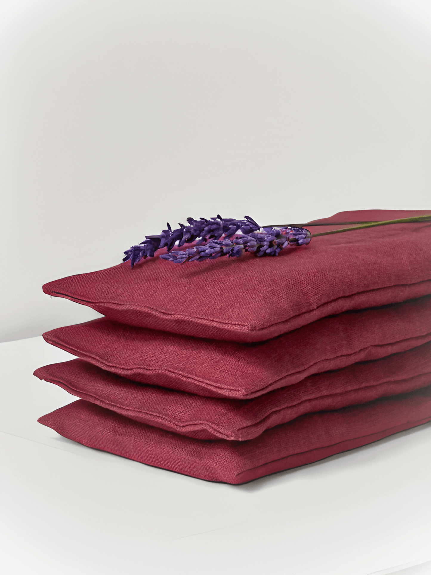 Stack of red linen eye pillows with a sprig of lavender on a white background