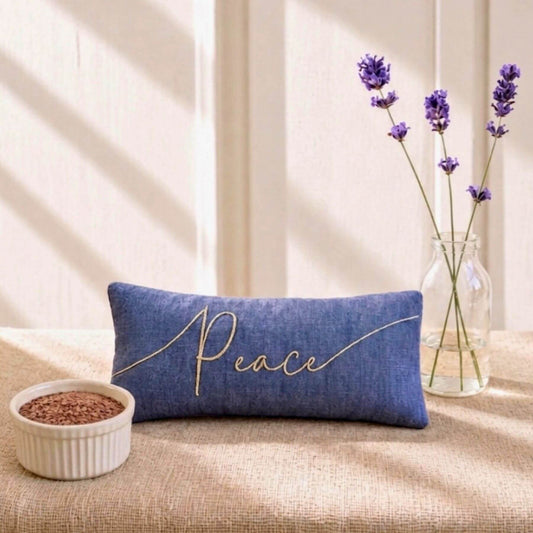 Blue eye pillow embroidered with 'Peace' text on a beige surface with a vase of lavender and small bowl of flaxseeds.